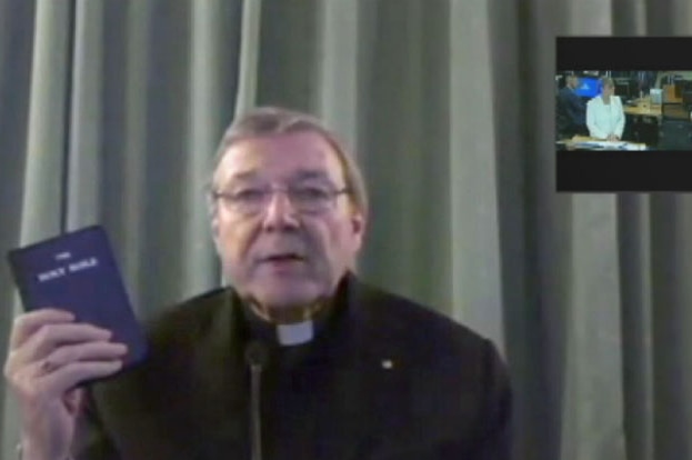 Cardinal George Pell sits in front of a curtain holding Bible before giving video evidence to the child abuse royal commission.