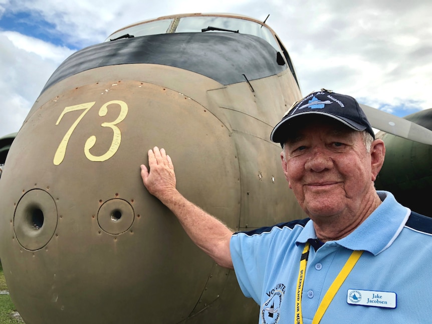 Man standing with his hand on the nose of a Caribou aircraft, smiling.