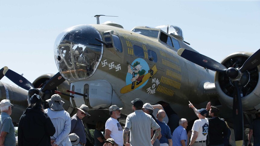 Plane fans crowd around a B-17 vintage WWII era Flying Fortress, painted olive green and with anti Nazi imagery