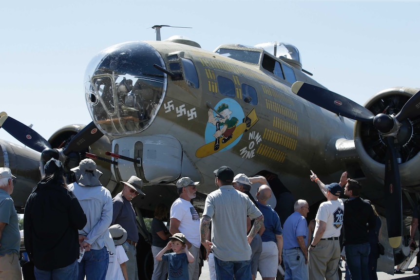 Plane fans crowd around a B-17 vintage WWII era Flying Fortress, painted olive green and with anti Nazi imagery