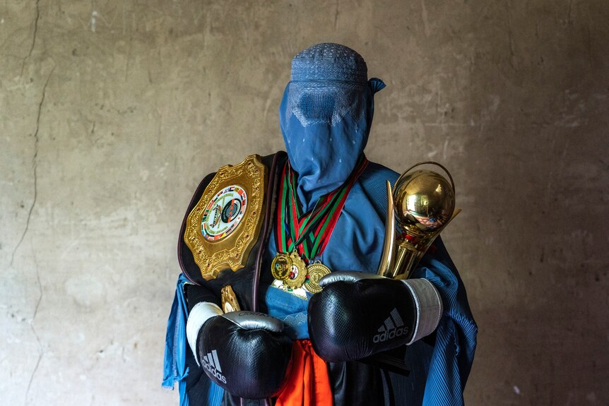Afghan mixed martial arts fighter poses for a photo wearing a burqa with her trophies.