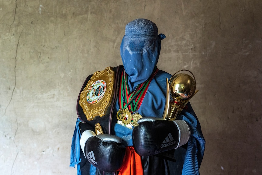 An Afghan mixed martial artist poses for a photo wearing a burqa with her trophies.