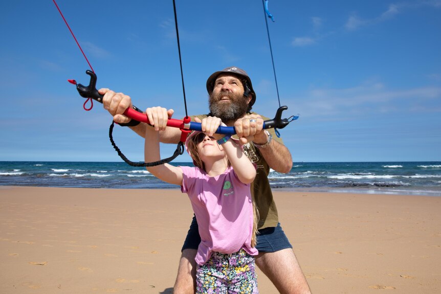 Man and his daughter enjoy kite surfing on the beach.