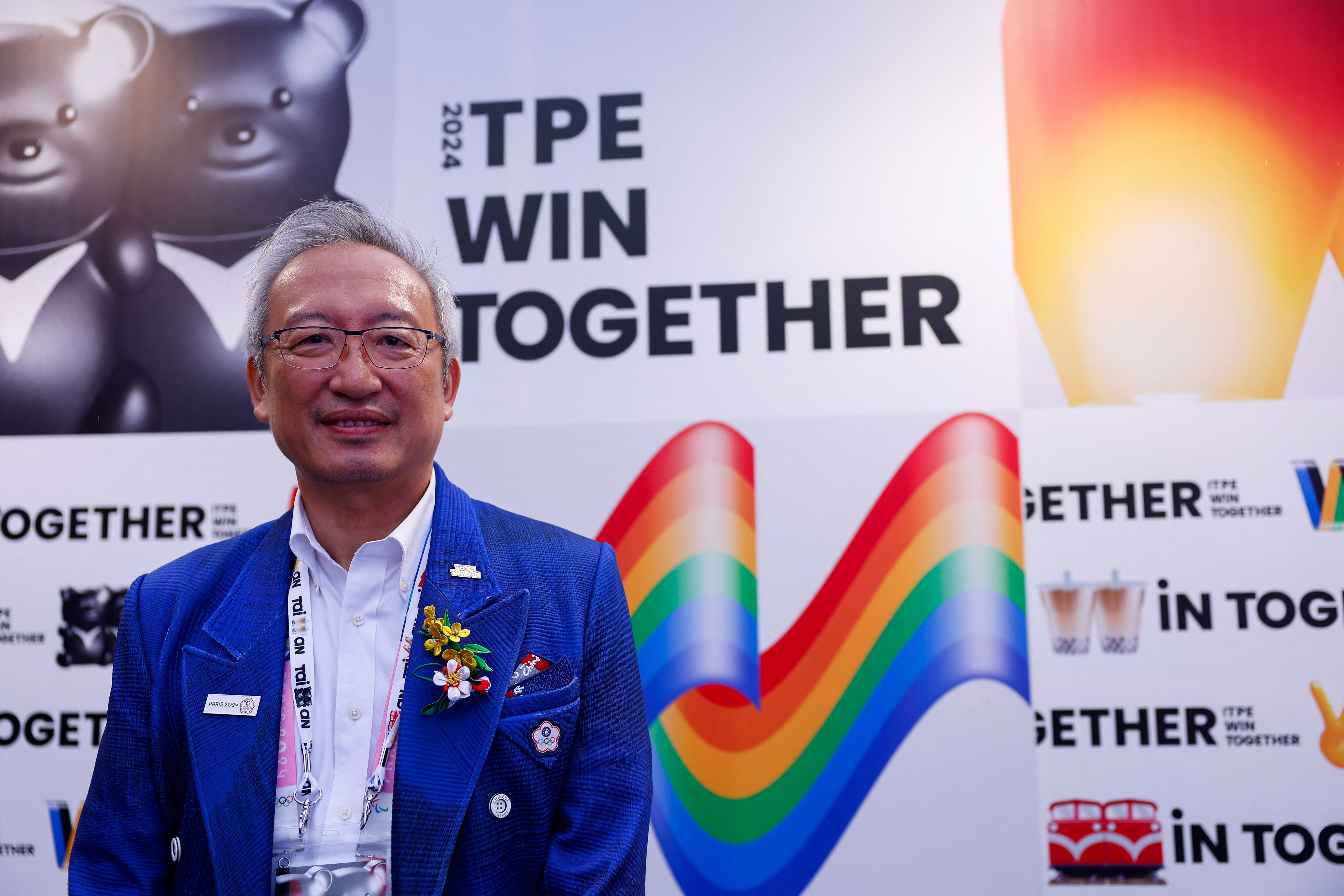A man in a blue jacked stands on a white backdrop with a rainbow flag.