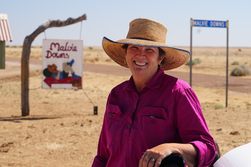 Grazier Gayle Batt wearing a deep pink workshirt smiles at camera leaning on bonnet of car