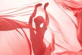 Billowing red sheets are held in front of a silhouette of a dancing female figure.