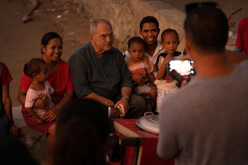 Two men and a woman sit with three small children while someone take a photo of them.