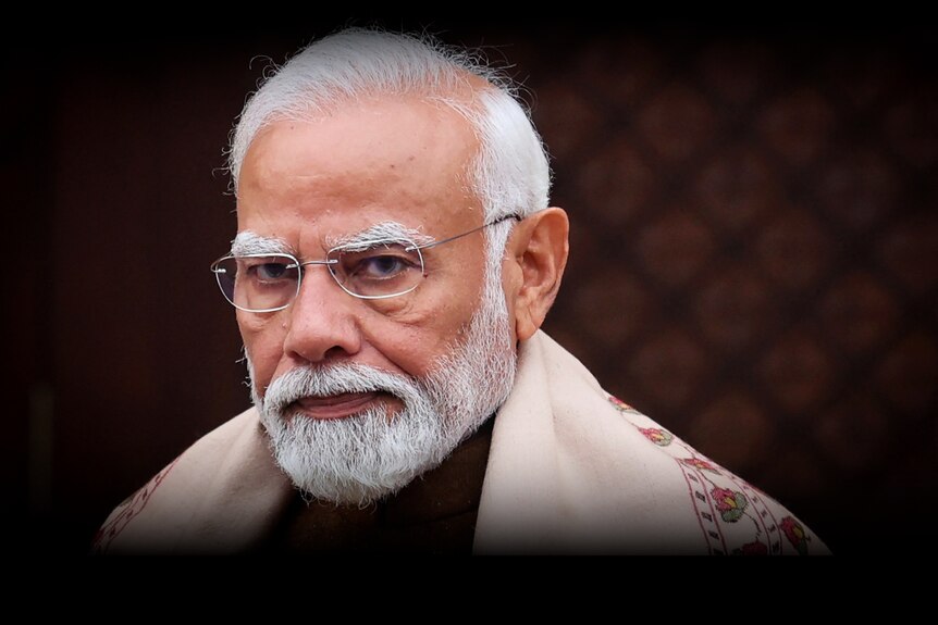 Narendra Modi looks directly into camera while wearing rimless glasses and a beige stole