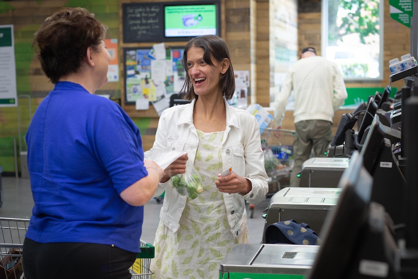 Two women standing and laughing at a supermarket checkout