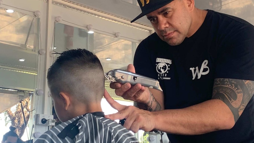 A man cuts the hair of a child in a mobile barber shop.