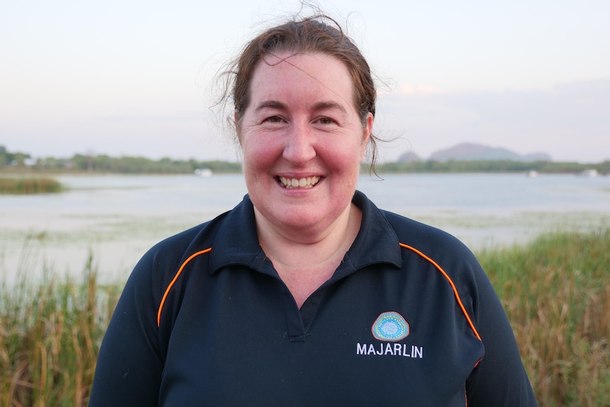 a woman smiles to a camera while standing in front of a lake