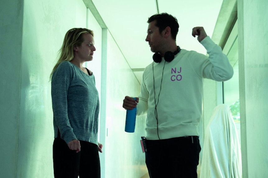 Leigh Whannell (R), wearing headphones, talks to Elisabeth Moss