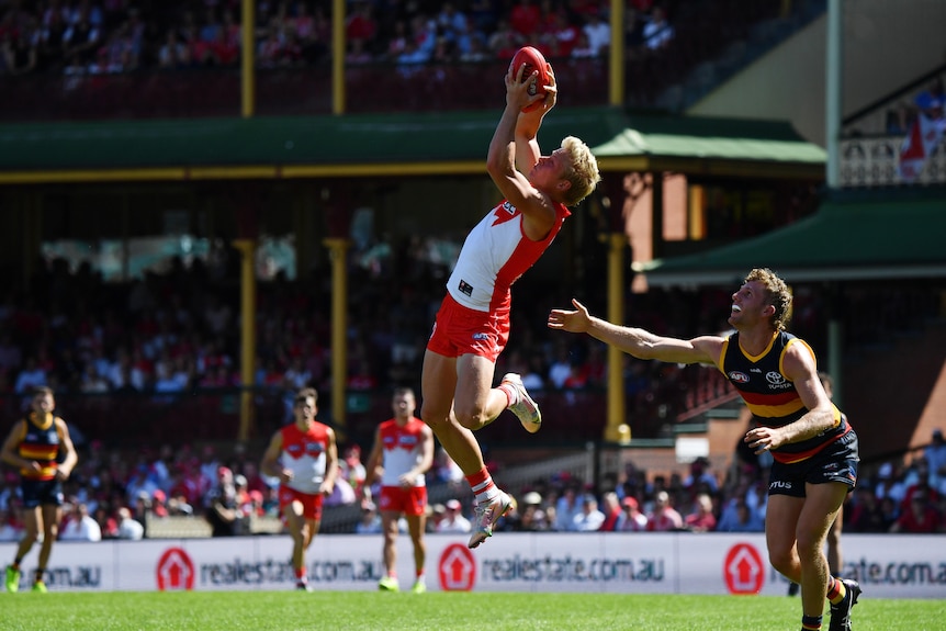 An AFL player leaps high to grab the ball while a defender watches.
