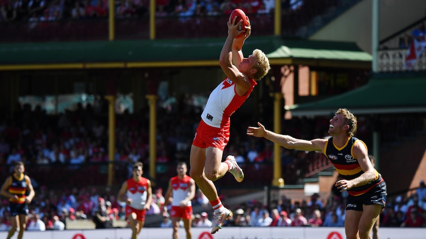 An AFL player leaps high to grab the ball while a defender watches.