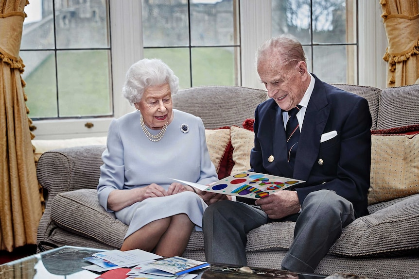 Queen Elizabeth II and Prince Philip smile as they read an anniversary card on a sofa