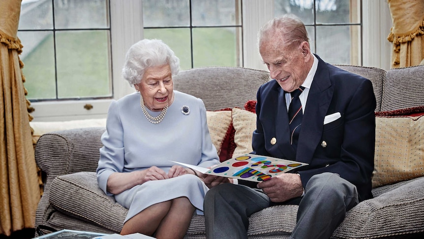 Queen Elizabeth II and Prince Philip smile as they read an anniversary card on a sofa