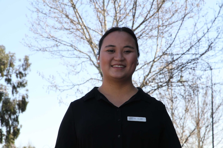 Bu Gay, a Karen social worker in Bendigo, looks at the camera. She's surrounded by blue sky and tree branches.