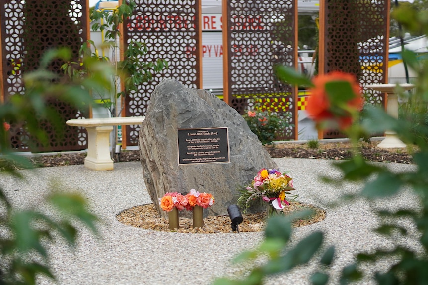 A memorial stone surrounded by flowers, behind it is a white bench