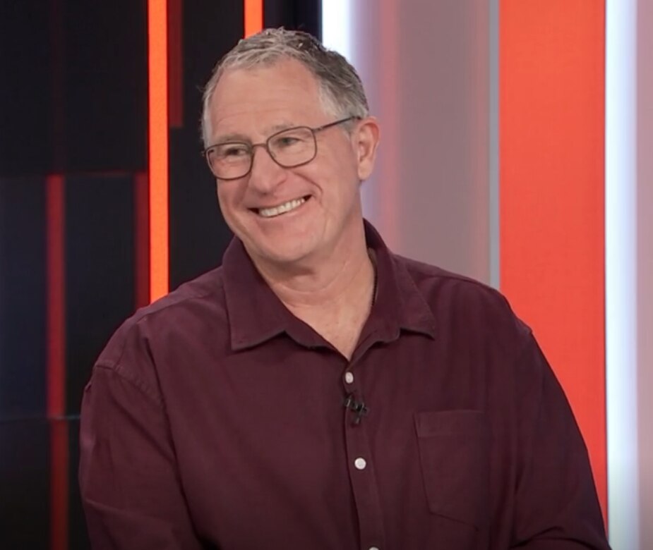 A man in glasses smiling on a panel show