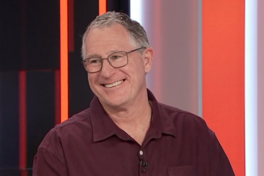 A man in glasses smiling on a panel show