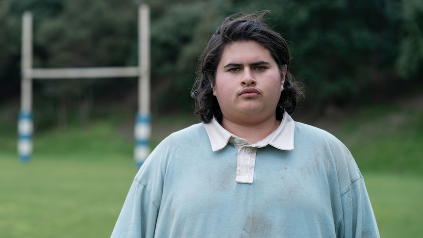 Julian Dennison wears a dirty rugby jersey and stares at the camera in Uproar.