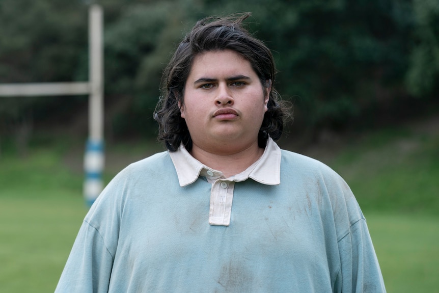 Julian Dennison wears a dirty rugby jersey and stares at the camera in Uproar.