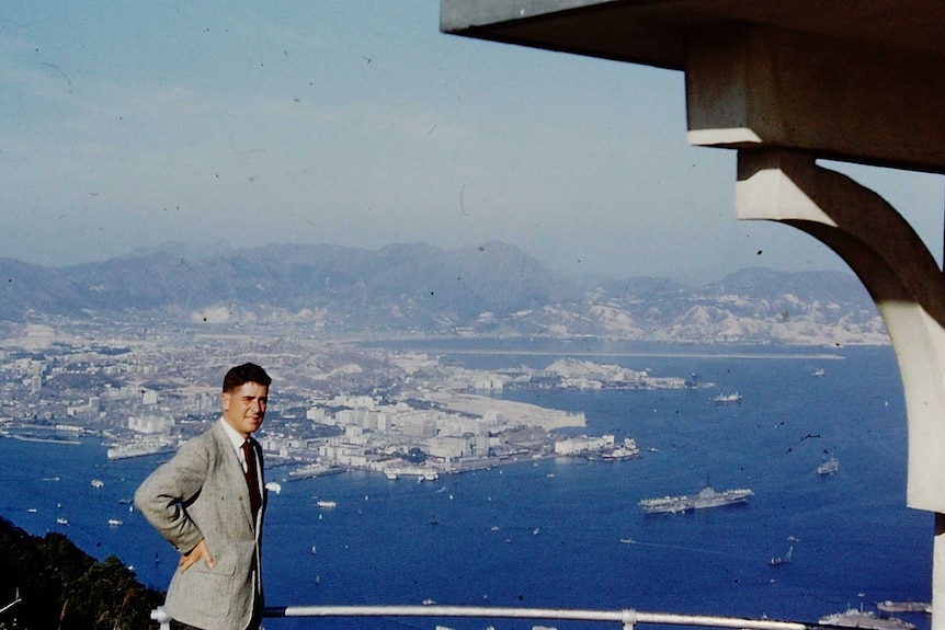 John Hamilton stands at a lookout with 1950s Hong Kong behind him