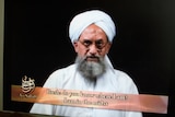 An open laptop displays a full-screen video of a bearded man in white turban speaking, with partial subtitles 