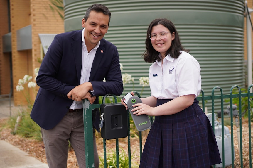 A man and a young girl stand next to a black locking box. The girl holds a phone in a grey pouch