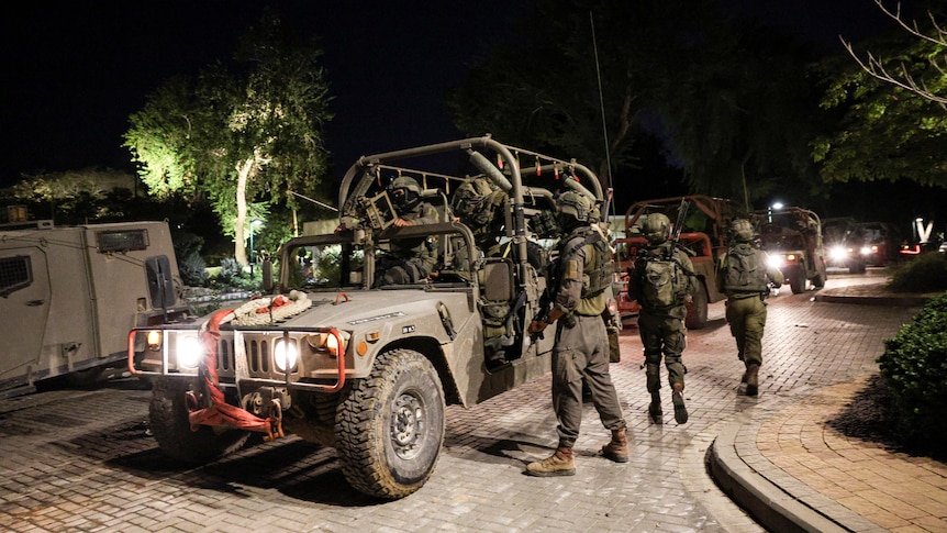 Israeli soldiers gather around a utility vehicle on a street at night