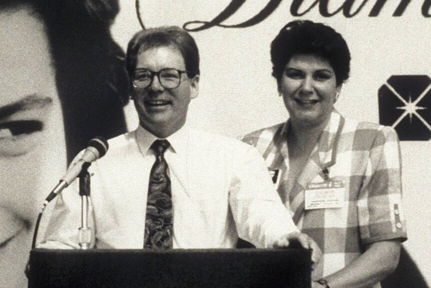 A black and white photo of a man and woman at a podium with a microphone.