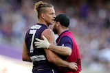 A Fremantle Dockers AFL player is assisted by a team staff member after being concussed.