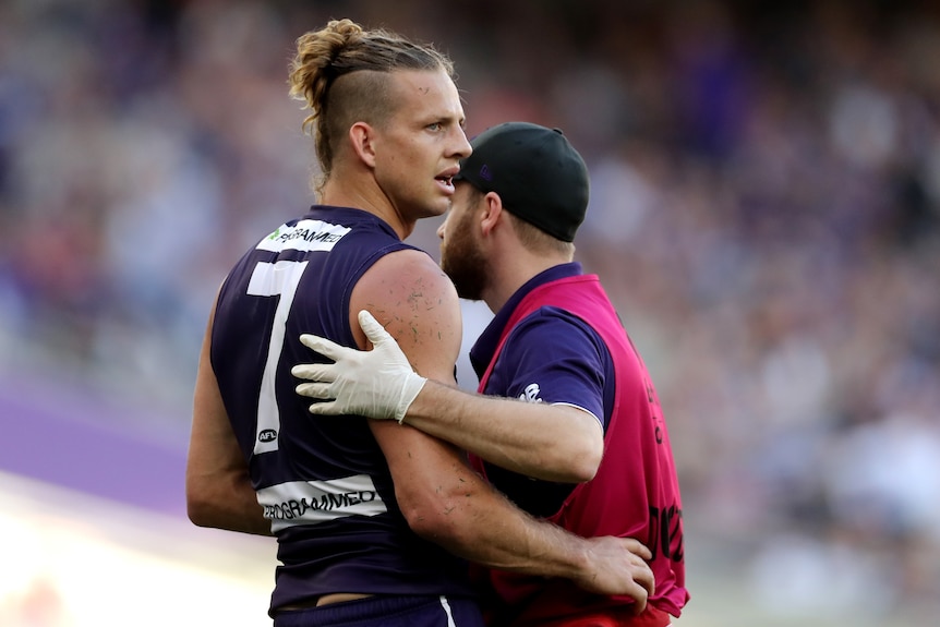 A Fremantle Dockers AFL player is assisted by a team staff member after being concussed.