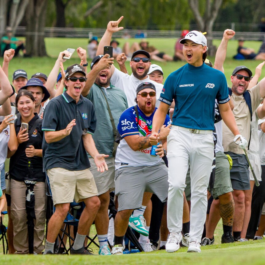 A male golfer celebrates cheering in front of a large group of fans 