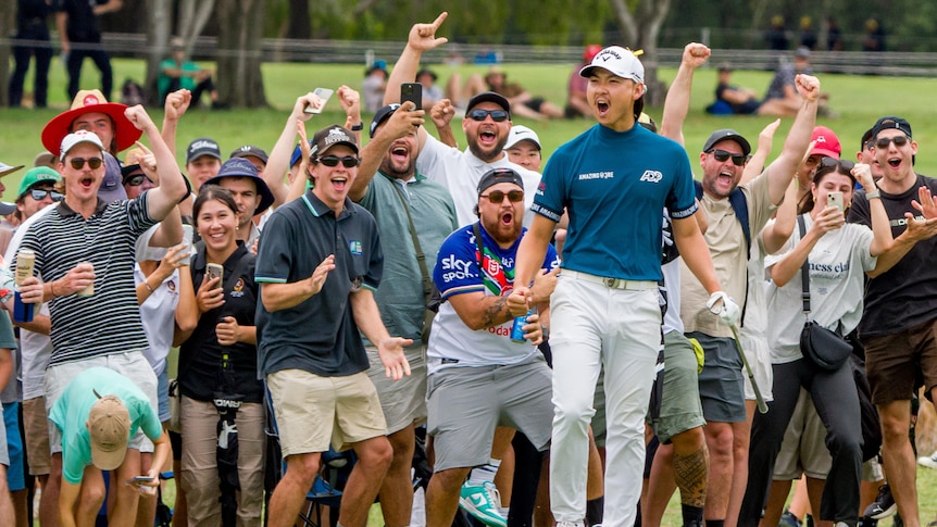 A male golfer celebrates cheering in front of a large group of fans 