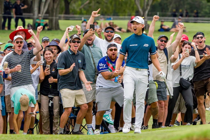 A male golfer celebrates cheering in front of a large group of fans 