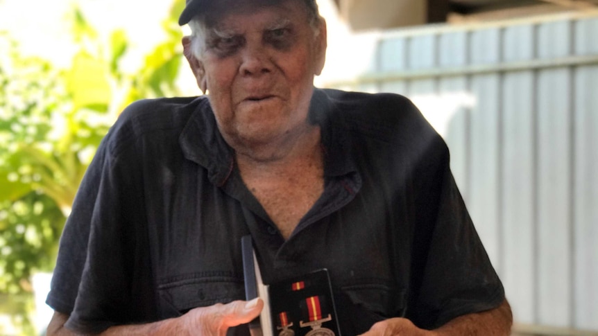 An elderly Indigenous man holding a medal