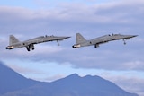Two F-5 fighter jets are see flying against a blue sky with white clouds.