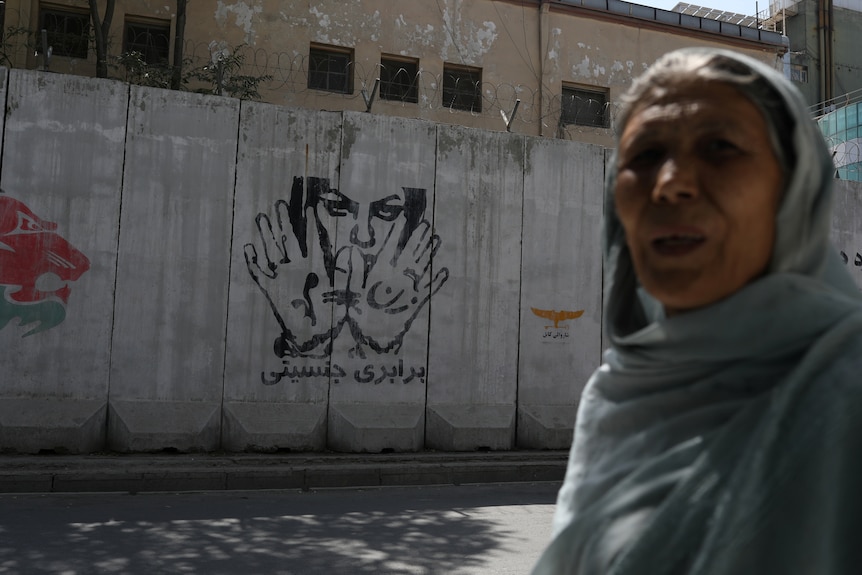 A mural reading "gender equality" is seen behind a woman in Kabul