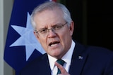 Scott Morrison stands infront of an Australian flag mid-sentence with his finger pointing