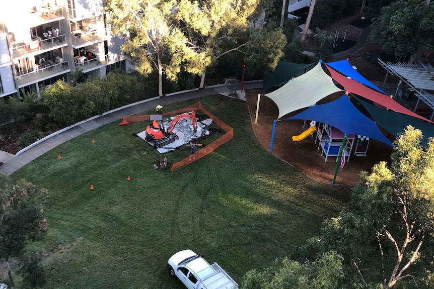 Council workers using an excavator to dig up a concrete slab in a park