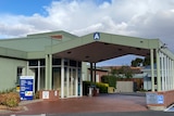A grene metal hospital building on a cloudy day. There is a sign and a letter A in blue