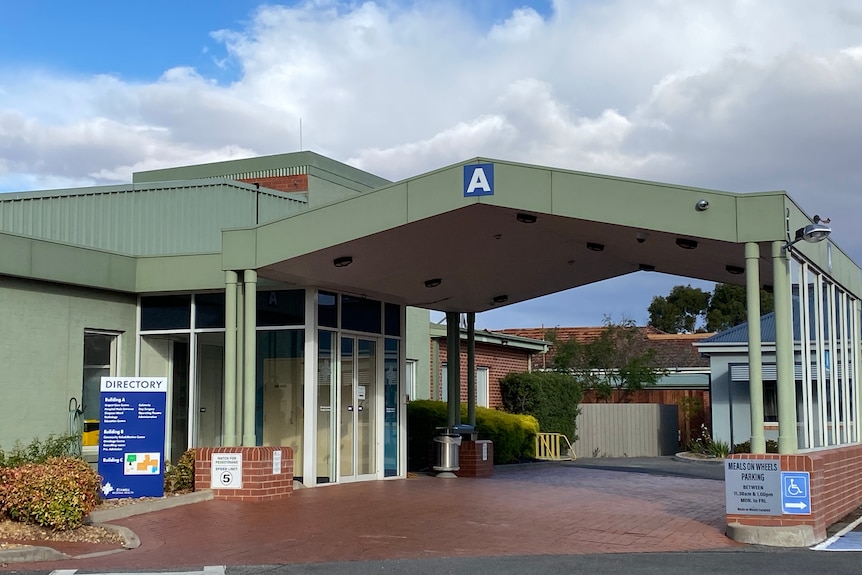 A grene metal hospital building on a cloudy day. There is a sign and a letter A in blue