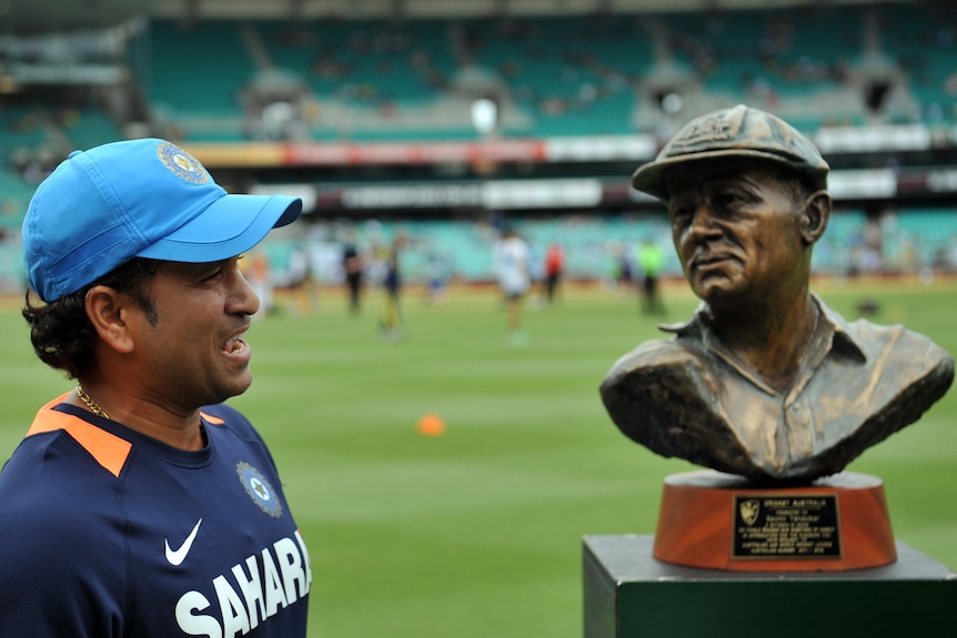 Indian cricketer Sachin Tendulkar smiles in his team gear as he stands next to a bronze bust of Sir Donald Bradman at the SCG. 