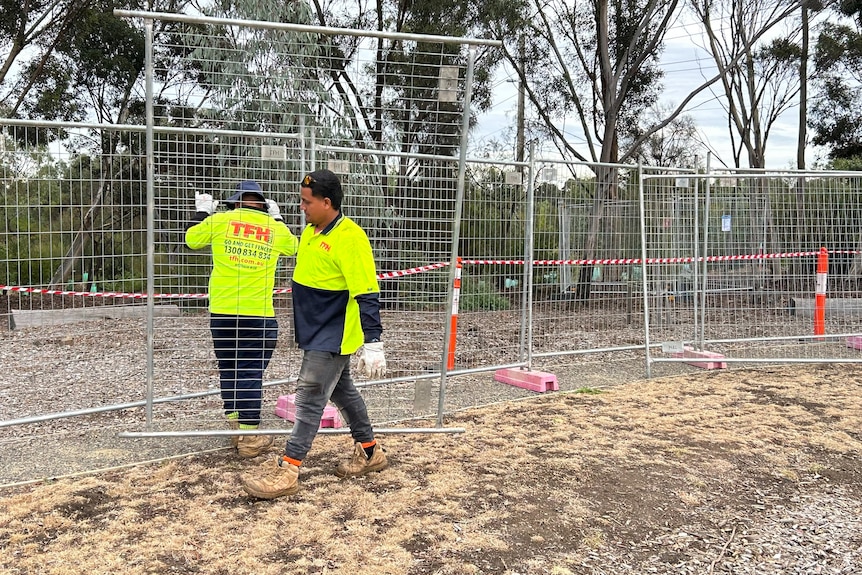 Two men in high visibility tops fence off a section of a park.