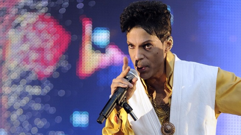 Prince performing on stage at the Stade de France in Saint-Denis, outside Paris, in yellow and white outfit.