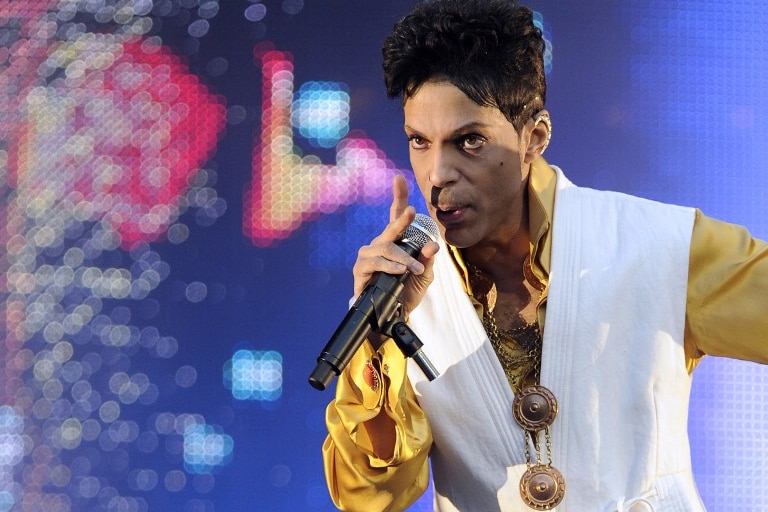 Prince performing on stage at the Stade de France in Saint-Denis, outside Paris, in yellow and white outfit.