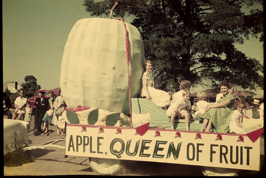 A woman sitting on a float with a large apple and children sitting around it
