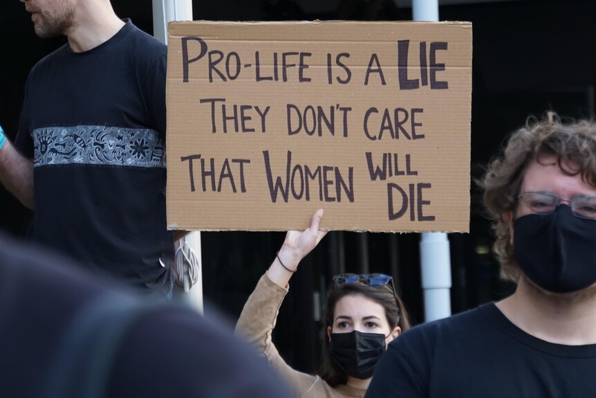 A woman holds up a sign saying 'Pro-life is a lie, they don't care that women will die'