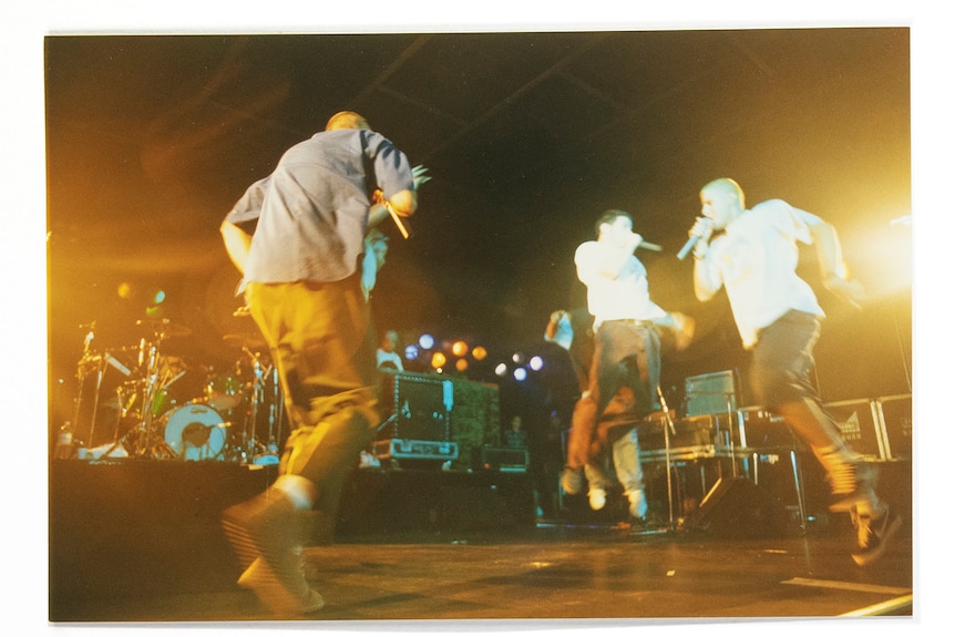 blurry photo of Beastie Boys performing live on stage. Three men rap into mics while jumping.